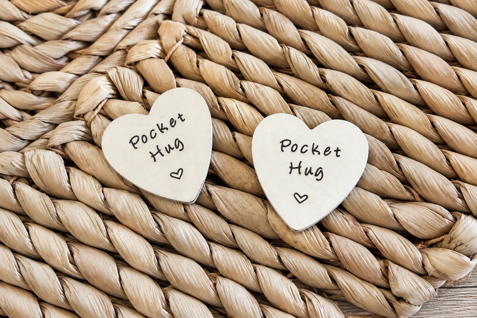 Two wooden pocket-hug hearts resting on a woven wicker surface