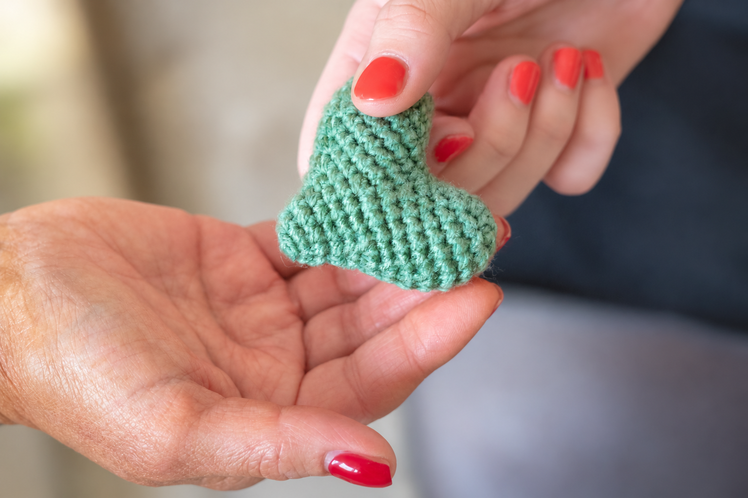 A small turquoise crocheted heart held gently between two hands