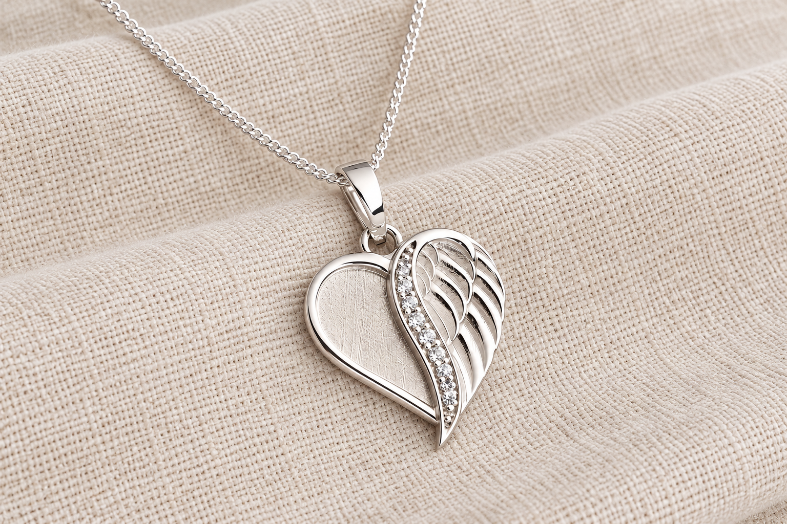 A silver heart pendant with a wing design on soft linen