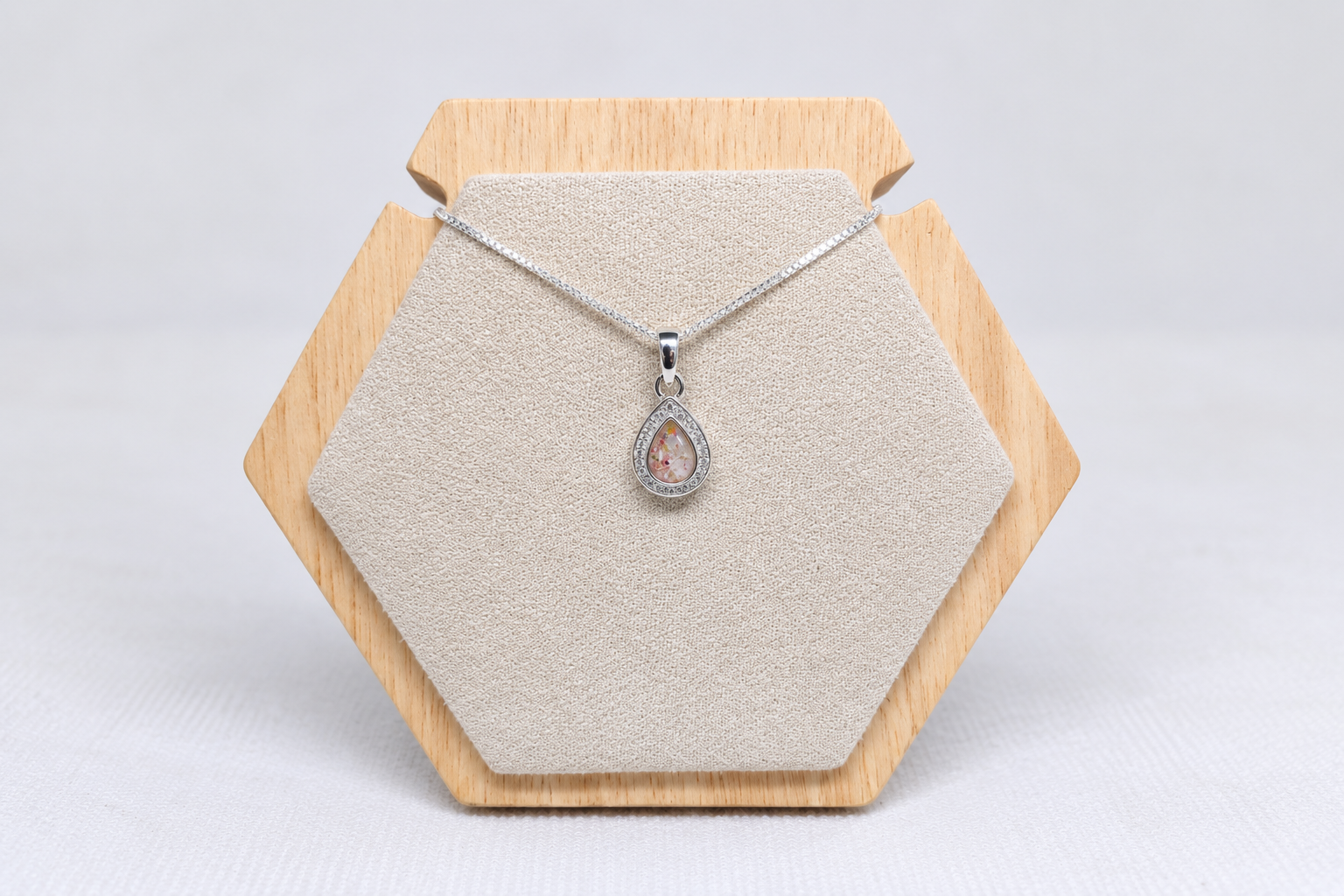 A silver teardrop pendant and chain on a wooden jewellery display