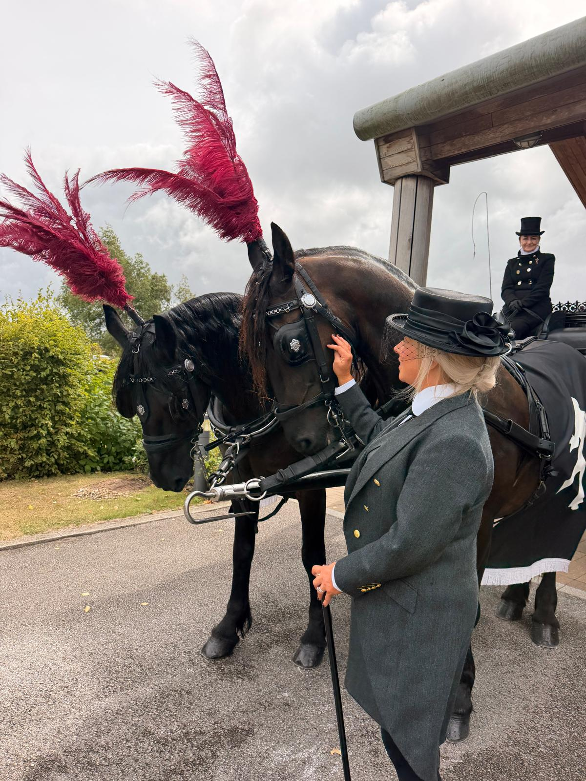 Funeral directors with two horses beside a traditional horse-drawn carriage