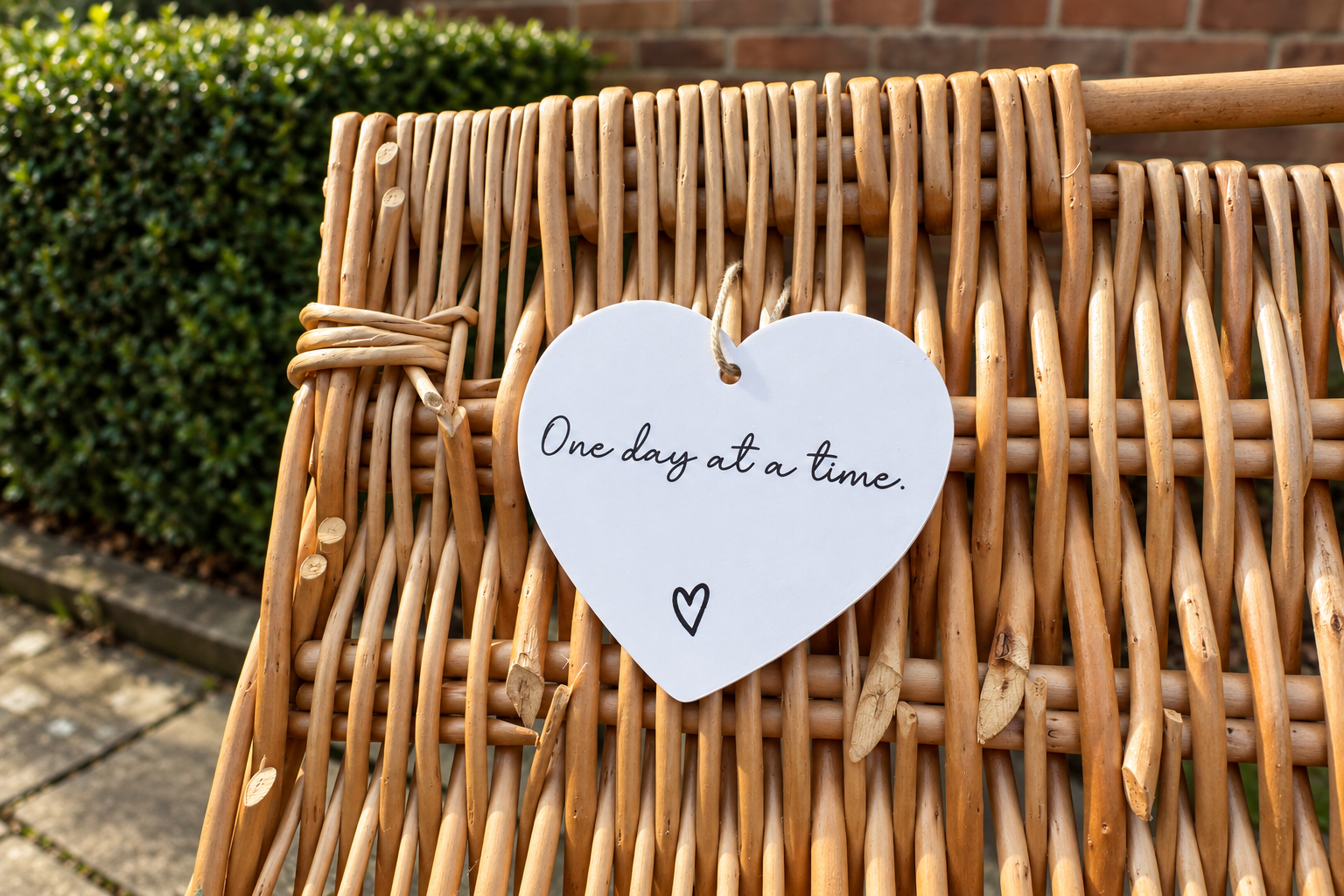 A white heart tag on a wicker chair reading One day at a time